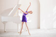 A cute little girl dreams of becoming a professional ballerina. In a white room, next to the piano, a girl in a lilac leotard is dancing on pointe shoes. Vocational school student.