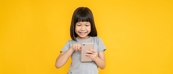 Wall Mural - Portrait of young fun smart happy little asian girl isolated on yellow studio shot. Education for elementary kindergarten, little girl hold mobile smart phone, online back to school concept.