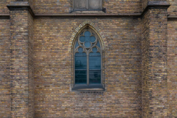 Ancient brick wall of a church with a large arched window.