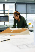Asian Young Female Architect Examining Architectural Model In Office