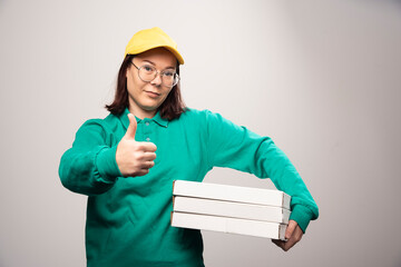 Wall Mural - Deliverywoman showing a thumb up and holding cardboards of pizza on a white background