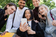 © LIGHTFIELD STUDIOS - Blurred asian student holding smartphone near interracial friends in park.