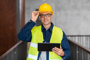 architecture, construction business and building concept - happy smiling male architect in helmet and safety west with tablet pc computer at office