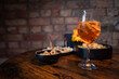 © Aerial Film Studio - Traditional italian aperitif with cheese, nuts and aperol spritz drink on the wooden table with blurred food on the background in a bar
