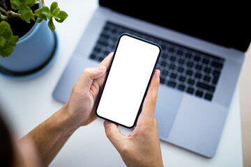 Wall Mural - Man using smartphone blank screen frameless modern  - top view, laptop keyboard in background