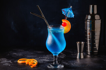 Wall Mural - gGass of blue lagoon cocktail decorated with orange and cherry at festive bar counter background.