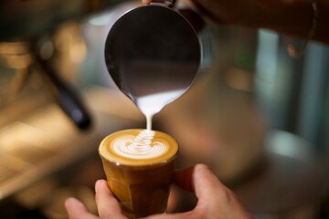 Shallow focus of a male hand pouring milk on a cappuccino for decoration