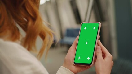 Over the sholder shot woman watching green screen phone on the underground. Woman using technology on the subway. Technology content.