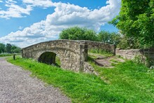 Small Stone Bridge In The Countryside All Covered In Greenery Next To The Road Under The Blue Sky