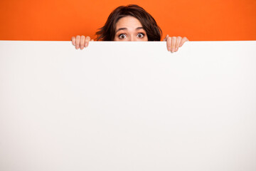 Poster - Portrait of puzzled person eye peeking behind empty space blank isolated on orange color background