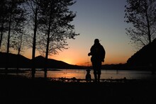 Man With A Dog Near The Lake During The Sunset