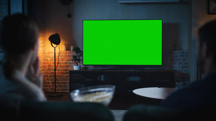 Aufkleber - Authentic Couple Spending Time at Home, Sitting on a Couch and Watching TV with Green Screen Mock Up Display in Their Stylish Loft Apartment. Man and Woman Streaming Movie or Show. Shot From Back.