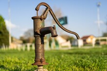Shallow Focus Of An Old Retro Hand Water Pump On A Blurred Grass Field