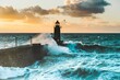 Large waves crash against the stone tower of the lighthouse at high tide at sunset