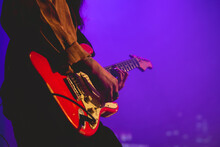 Closeup Of Young Latino Guitar Player With Shirt And Red Guitar Playing Live In A Concert Under Colorful Lights