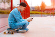 Young hipster guy skateboarder selfie with mobile phone while sitting on skateboard outdoors
