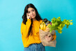 © luismolinero - Young woman holding a grocery shopping bag isolated on blue background thinking an idea