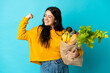 © luismolinero - Young woman holding a grocery shopping bag isolated on blue background doing strong gesture