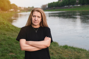 A woman against the background of nature, the river stands with a stern, slightly angry look, she needs to go home to cook, clean house, but she doesn't want to, she wants peace and rest