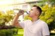 © Евгений Шемякин - Portrait of handsome guy, young happy thirsty man runner is drinking pure fresh water from plastic bottle at warm sunny summer day outdoors after running, jogging, training outside. Side profile view