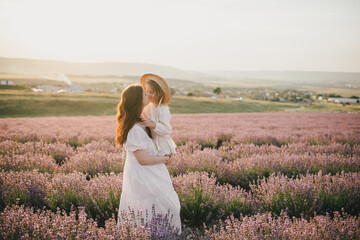 Happy mother and daughter wearing white vintage dresses having fun in lavender field at sunset.