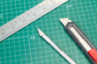 © Mercedes Fittipaldi - Bisturí de acero, cutter y regla metálica sobre una tabla de cortar verde. Vista superior y de cerca. Copy space