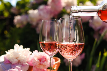 Pouring rose wine into glass in garden, closeup