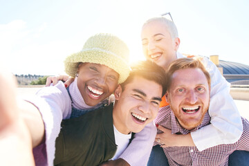 Piggyback friends taking smiling selfie together outdoors in a sunny day. Self portrait of a group of young people having fun together. Guys and Girls looking at camera posing for the photo