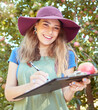 © Jade M/peopleimages.com - Portrait of female farm worker holding an apple while writing and making notes on a orchard farm during harvest season. Agronomist doing inspection and record keeping on the quality of produce