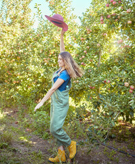 Wall Mural - Cheerful farmer feeling optimistic and fulfilled for harvest season of fresh organic fruit. One excited energetic happy young woman jumping for joy on sustainable apple orchard farm on sunny day.
