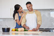© Beaunitta V W/peopleimages.com - A young loving latin couple cooking a healthy dinner together at home. A loving man cutting carrots and other vegetable foods, preparing a meal and his girlfriend holds him and smiles in the kitchen