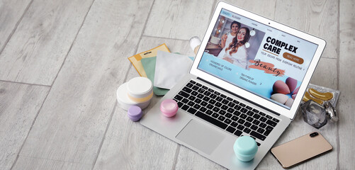 Laptop with open page of beauty blog, mobile phone and cosmetic products on light wooden floor with space for text