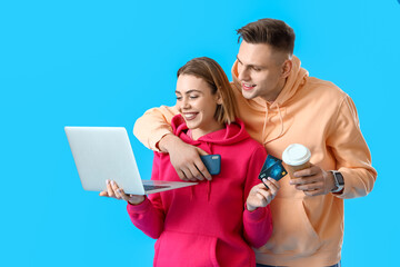 Young couple with laptop, credit cards and cup of coffee on blue background. Online shopping