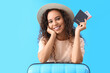 Young African-American woman with passport and suitcase on blue background