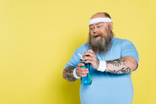 Thirsty Overweight Man With Beard Opening Sports Bottle Isolated On Yellow.