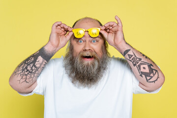 Wall Mural - amazed tattooed plus size man holding glasses with sale lettering isolated on yellow.