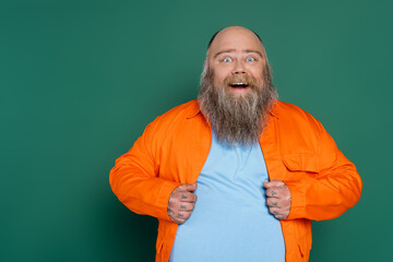 Wall Mural - amazed overweight man with beard looking at camera isolated on green.