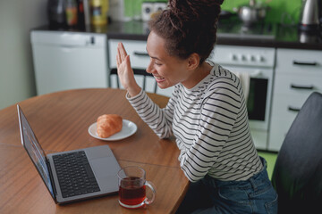 Wall Mural - side view of mixed-race cheerful female student waving hand having video conversation online