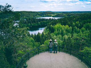 Wall Mural - A young couple from back on the observation deck among blue lakes and green forests in summer Finland.