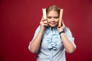 Wall Mural - Blonde studentgirl holds her books and covers her ears with them