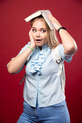 Wall Mural - Young blonde schoolgirl holds her book at her head and looks tired and confused