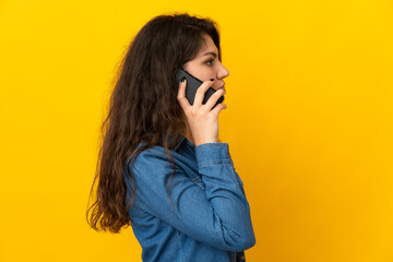 Wall Mural - Teenager Russian girl isolated on yellow background keeping a conversation with the mobile phone with someone