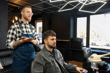 Wall Mural - Professional hairdresser working with bearded client in barbershop