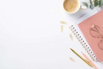 Business concept. Top view photo of workplace pink notepads glasses cup of coffee clips pens and eucalyptus on isolated white background with empty space