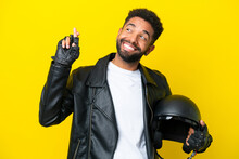 Young Brazilian Man With A Motorcycle Helmet Isolated On Yellow Background With Fingers Crossing And Wishing The Best