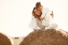 Mom And Son Are Sitting On A Haystack In The Field At Sunset