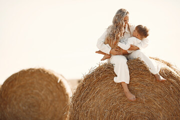 Mom and son are sitting on a haystack in the field at sunset