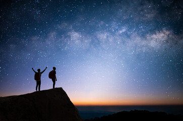 Wall Mural - Silhouette of two young man standing, open arms and watched the star, milky way and night sky on top of the mountain. They enjoyed traveling and was successful when he reached the summit.