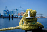 Fototapeta  - A iron bollard with a tied rope on a quay in the Port of Rotterdam in the Netherlands. In the background, slightly out of focus, is the industrial area of the Maasvlakte near Rotterdam.