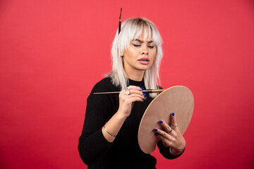 Young artist woman holding art supplies on a red background